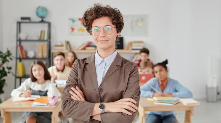 A confident teacher stands in front of students in a classroom setting.