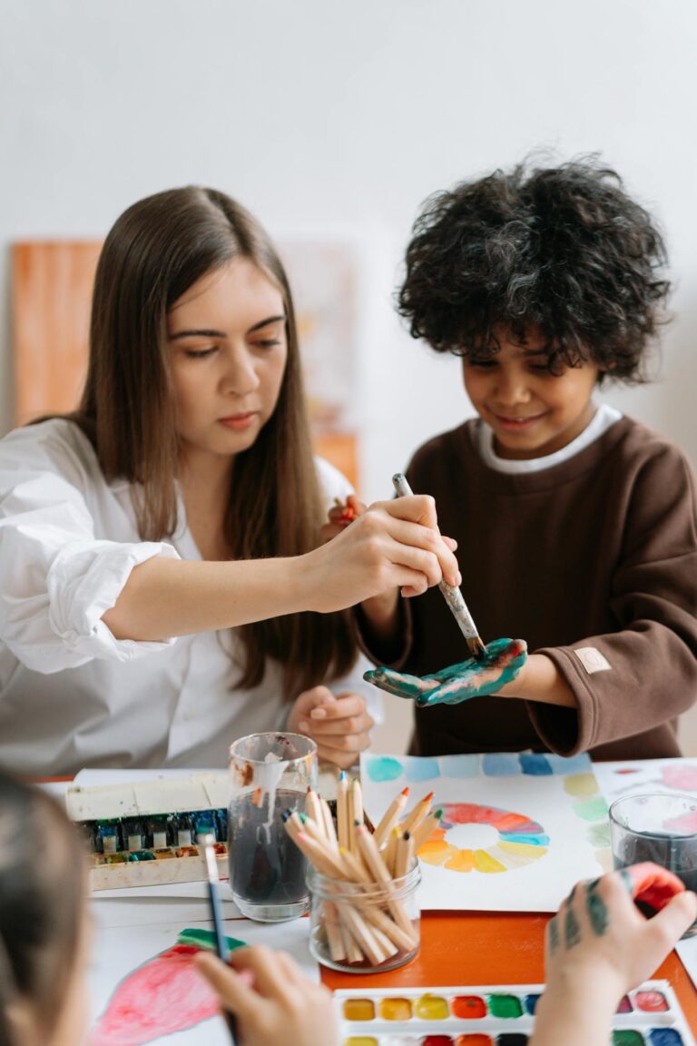 A teacher and child painting with brushes and watercolors in a creative classroom setting.